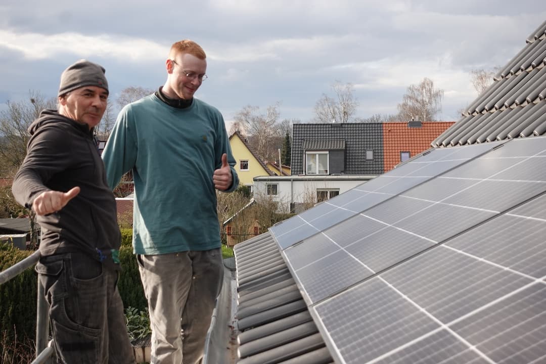 Zwei Personen zeigen Daumen hoch neben einer PV-Anlage